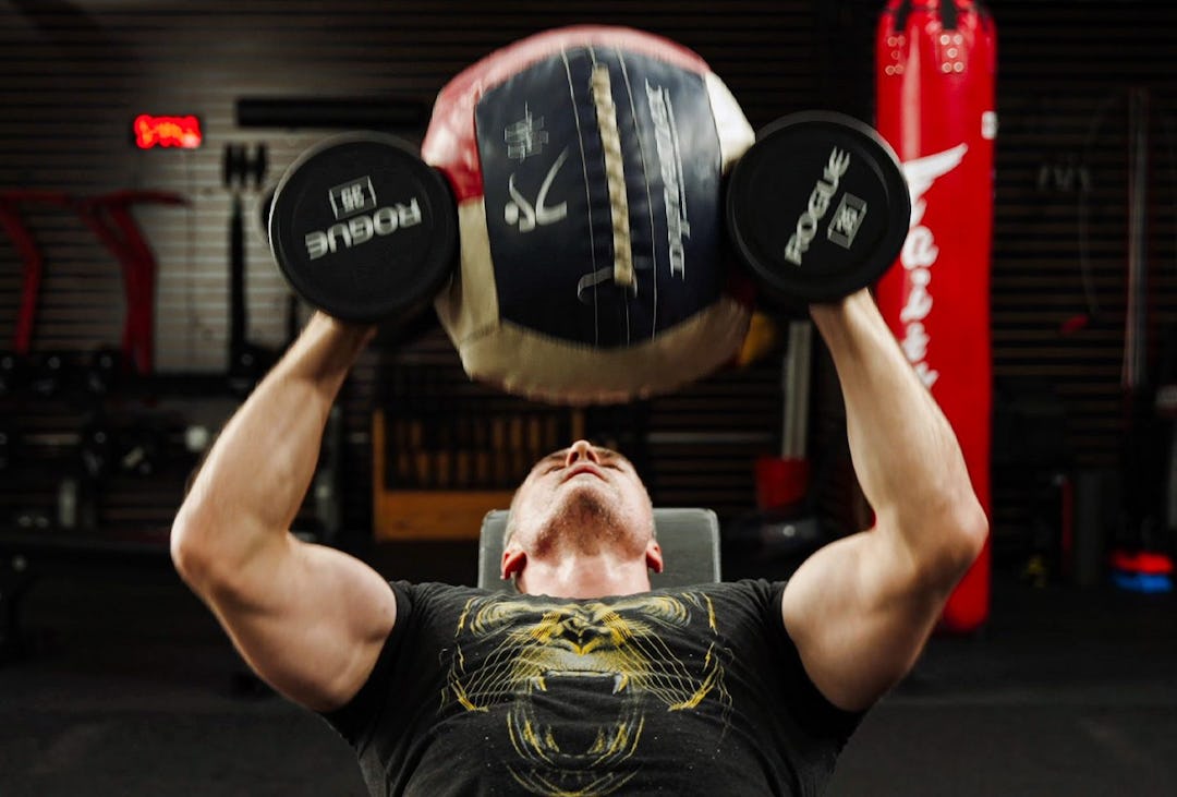 Man performs dumbbell hex press with medicine ball